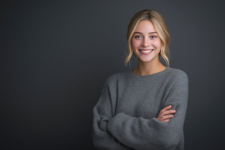 A cheerful and confident woman with blue eyes and a friendly smile stands against a dark gray background. A positive and professional studio portrait.の素材