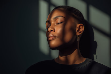 A serene African American woman with a short haircut enjoys a moment of peace, her eyes closed as sunlight casts the shadow of prison bars on her skin.の素材