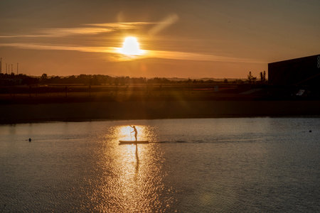 Silhouette of men on sup board with oar in hands on lake in evening with magnificent sunset in background. Active lifestyle. Expano, Murska Sobota, Sloveniaの写真素材
