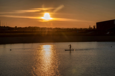 Silhouette of men on sup board with oar in hands on lake in evening with magnificent sunset in background. Active lifestyle. Expano, Murska Sobota, Sloveniaの写真素材