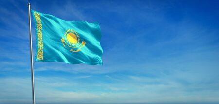 The National flag of Kazakhstan blowing in the wind in front of a clear blue skyの写真素材