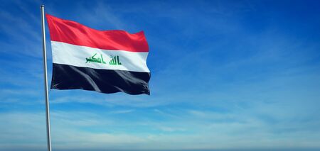The National flag of Iraq blowing in the wind in front of a clear blue skyの写真素材