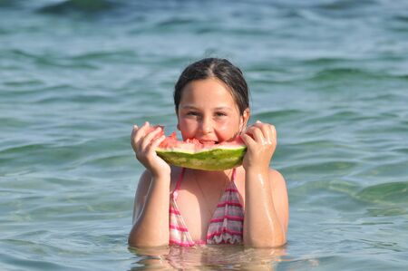 Girl eating watermelon on seashoreの写真素材
