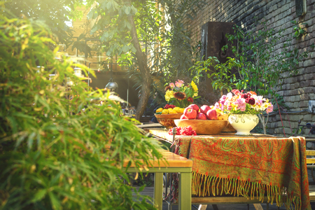Nicely decorated wooden table full of different kinds of fruits inside shiny beautiful garden with lots of flowers and green foliage aroundの写真素材