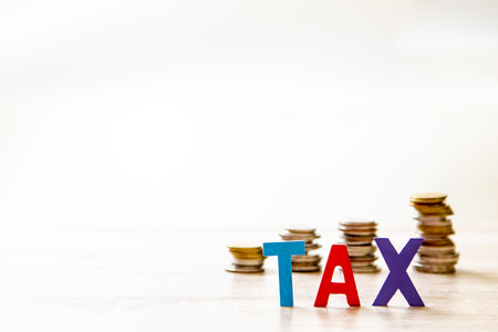 Tax concept. Word "TAX" alphabet made from wood  with blurred stack coins.の写真素材