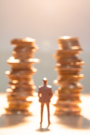 Out of focus ,behind a miniature of man standing with stack of coins.の写真素材