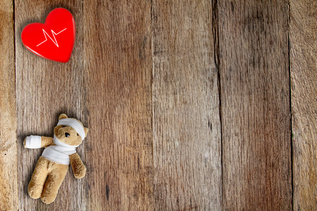 Teddy bear with bandage and red heart ball with heartbeat on wooden table form top view.の写真素材