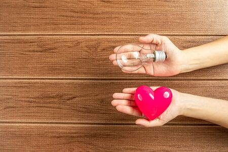 Hand holding a light bulb and pink heart with wooden background. Green energy concept ,Using environmentally friendly appliances concept.の写真素材