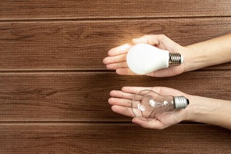 Hand holding a turned on LED light bulb on wooden background. Green energy concept, Using environmentally friendly appliances concept.の写真素材