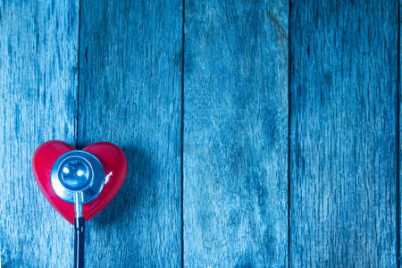 Red heart ball and stethoscope on wooden table.