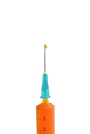 closeup photo of syringe with blue plastic cap and steel needle with red reflection and filled with orange liquid pouring out and falling down isolated on white background の写真素材