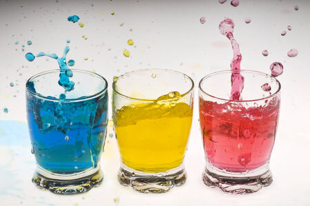 Three glasses with colored water splashing all around の写真素材