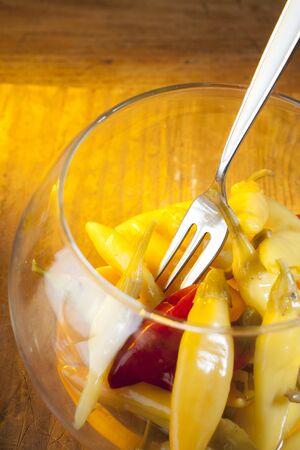 studio shot of yellow with one red pepperoni with glittering fork in oval glass bowl on wooden backgroundの写真素材