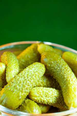 pickles in a glass oval jar on a wooden table with a green color backgroundの写真素材