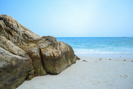Huge stone on white sand with blue ocean and blue sky background.の写真素材