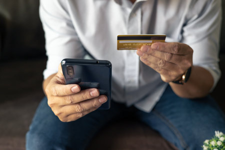 Man holding credit card and using smartphone at home, businessman shopping online, e-commerce, internet banking, spending money, working from home concept, Sit on the sofa in the living room at home.の写真素材