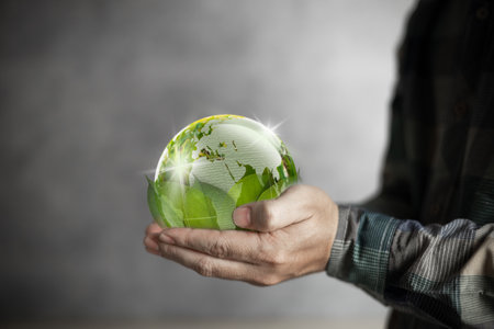 earth day Human hand holding a green world backed by leaves, conservation and environment concept.の写真素材