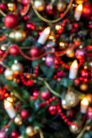 Green New Year tree decorated with toys, balls and candles. Defocused christmas background