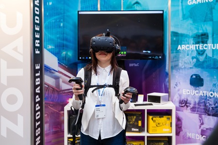 Hannover, Germany - March, 2017: Girl playing video game in virtual reality headset and handheld controllers developed by HTC Vive on exhibition Cebit 2017 in Hannover Messe, Germanyのeditorial素材