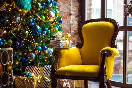 Dark room with Christmas and New Year interior decoration. Green tree decorated with toys and flashing garland and yellow chairの写真素材