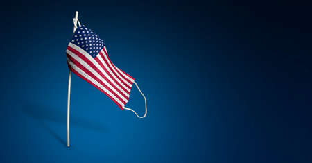 American mask on dark blue background. Waving flag of USA painted on medical mask on pole. Virus...
