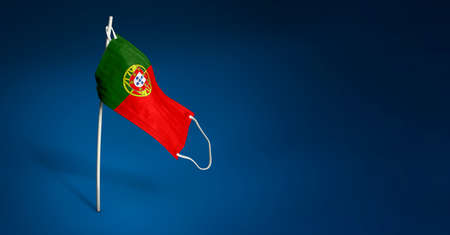 Portugal mask on dark blue background. Waving flag of Portugal painted on medical mask on pole....
