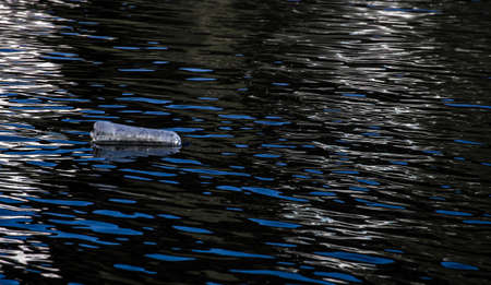 Plastic empty water bottle as pollution litters out waterways , plastic bottle floats on top of the dark waters on riverの写真素材