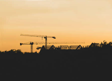 Lots of tower cranes build high-rise residential building in evening time. Steel frame structure in...