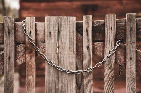 Old wooden gate closed with a rusty chain. Retro wood fence with vintage metal decorative elements. Rural backgroundの写真素材
