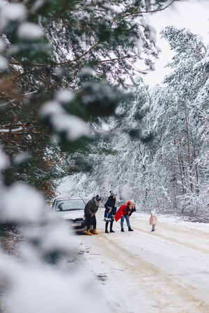 fun company with a little baby on a snowy road under winter pine trees stopped and walk around the carの写真素材