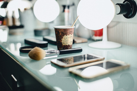 a cup of coffee and a make-up brush on the wizards table in the backlight on a glass surface with blemishesの写真素材