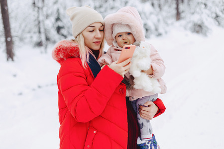 mom holds the baby in her arms and makes the selfie in the snowy area fun and tender