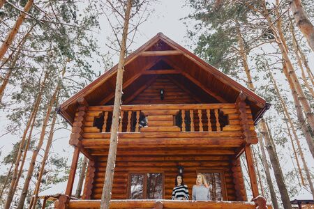 the girls came out of a cottage wooden house on the background of snow-covered pine treesの写真素材