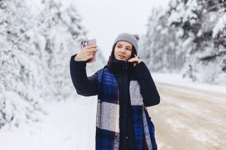 A pretty girl makes a selfie in the middle of a snowy forest road in winter