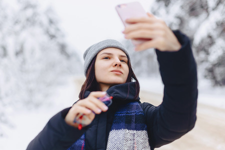 A pretty girl makes a selfie in the middle of a snowy forest road in winter