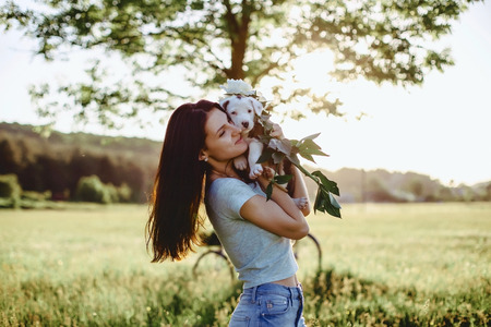 The girl walks with a puppy in a field in a bicycle in the back of warm, sunny lightの写真素材