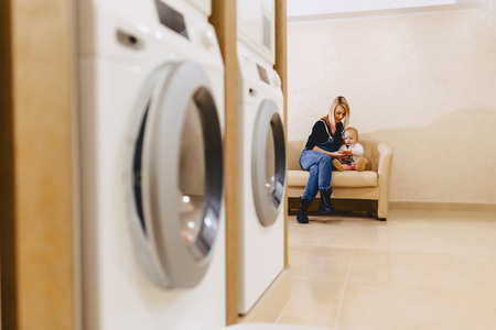 A woman with a child is sitting on the sofa in the laundry in the waiting for clothesの写真素材