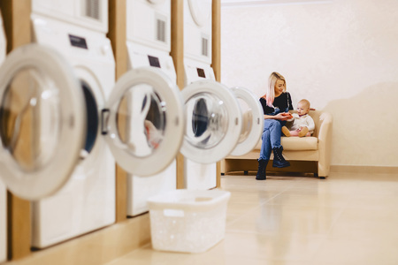 A woman with a child is sitting on the sofa in the laundry in the waiting for clothesの写真素材