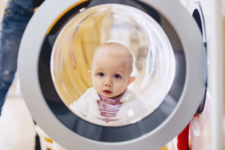 The baby looks through the window of the washing machine and laughs