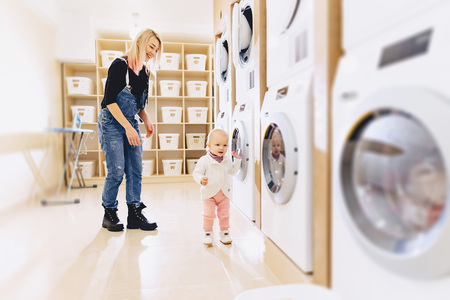a little girl with her mother throws clothes in the washing machine with funの写真素材