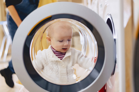 The baby looks through the window of the washing machine and laughsの写真素材