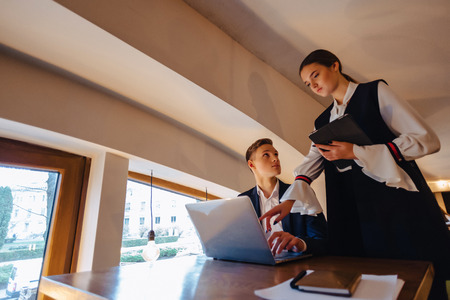 young businessmen boy and girl work with a laptop, a tablet and notes in the cafe with cozy interior