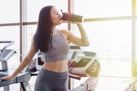 Girl in the gym are trained on treadmill and drink water, smiling and healthy