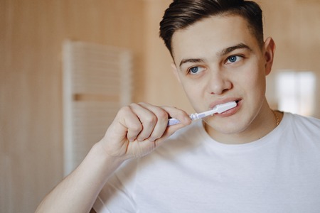 morning hygiene, the boy brushes his teeth near the mirror in the bright bathroom