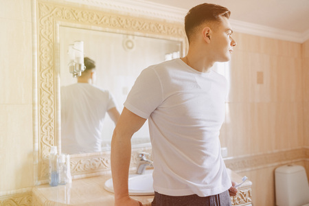 morning hygiene, the guy leaned on the washbasin in the bright bathroomの写真素材