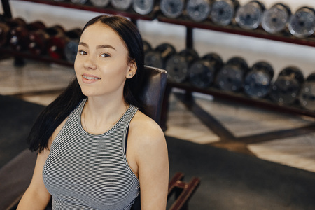 A young girl wearing sportswear in a gym performs dumbbell exercises, the coach helps her, sports, healthy lifestyleの写真素材