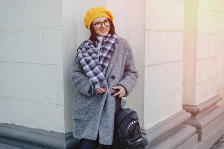 Attractive smiling young girl in stylish glasses in coat and yellow Beret on a simple light backgroundの写真素材