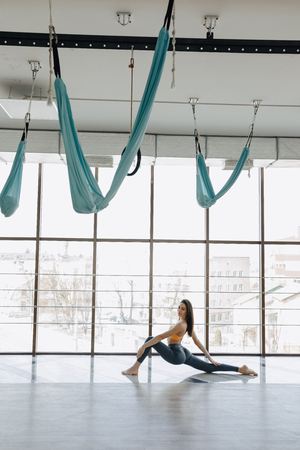 cozy young attractive girl doing fitness exercises with yoga on the floor against the background of panoramic windowsの写真素材