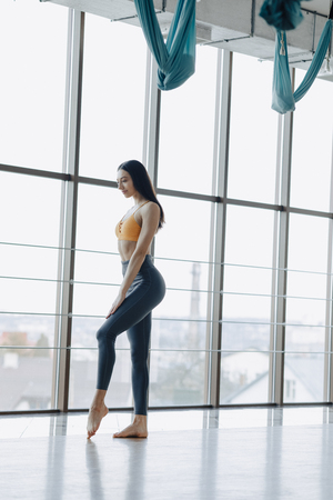 cozy young attractive girl doing fitness exercises with yoga on the floor against the background of panoramic windowsの写真素材