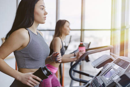 Girls in the gym are trained on treadmills and drink water, smiling and healthy